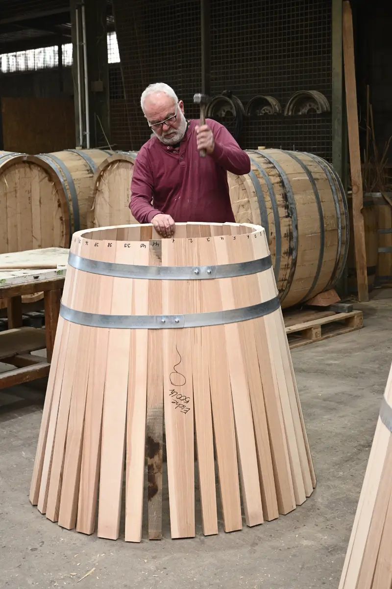 Ein älterer Küfer mit weißen Haaren der an einer Fassrose arbeitet.